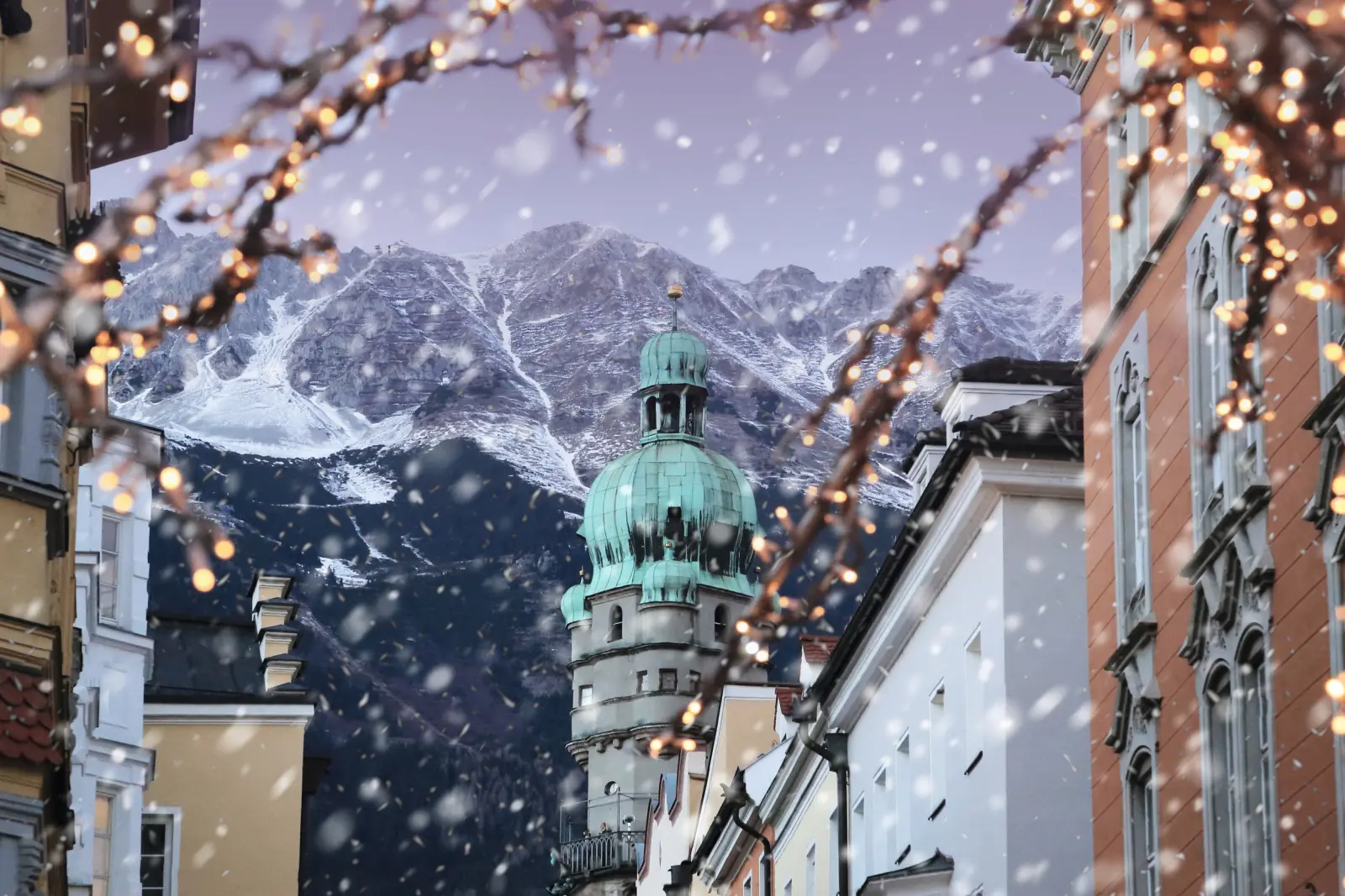 Snow-covered old town with a mountain backdrop and a tower in the background at dusk.