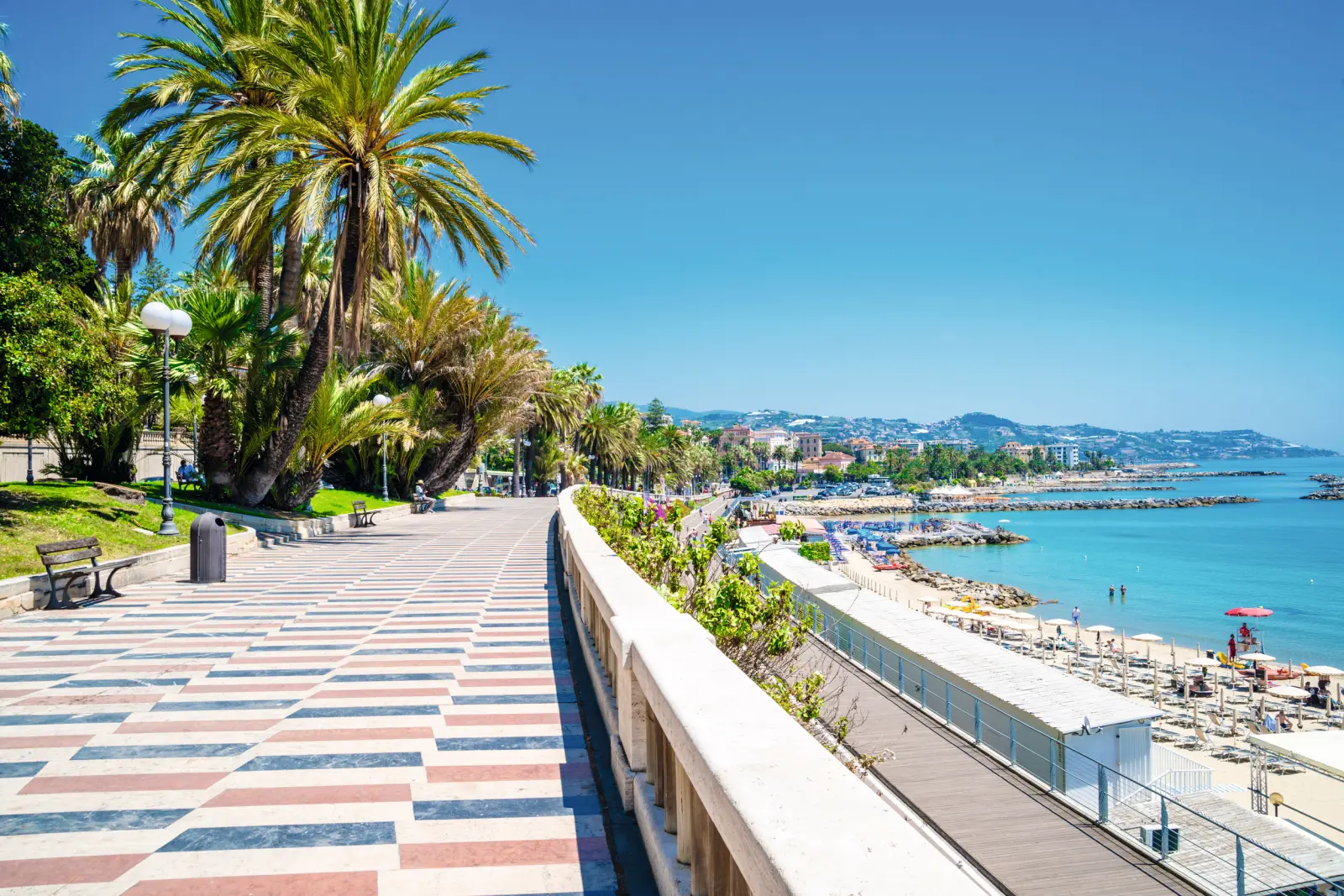 Promenade du bord de mer bordée de palmiers, avec vue sur la mer par temps ensoleillé.