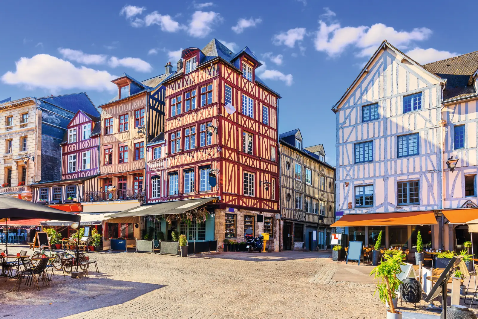 Historic half-timbered houses on a sunny square with cafés and blue sky.
