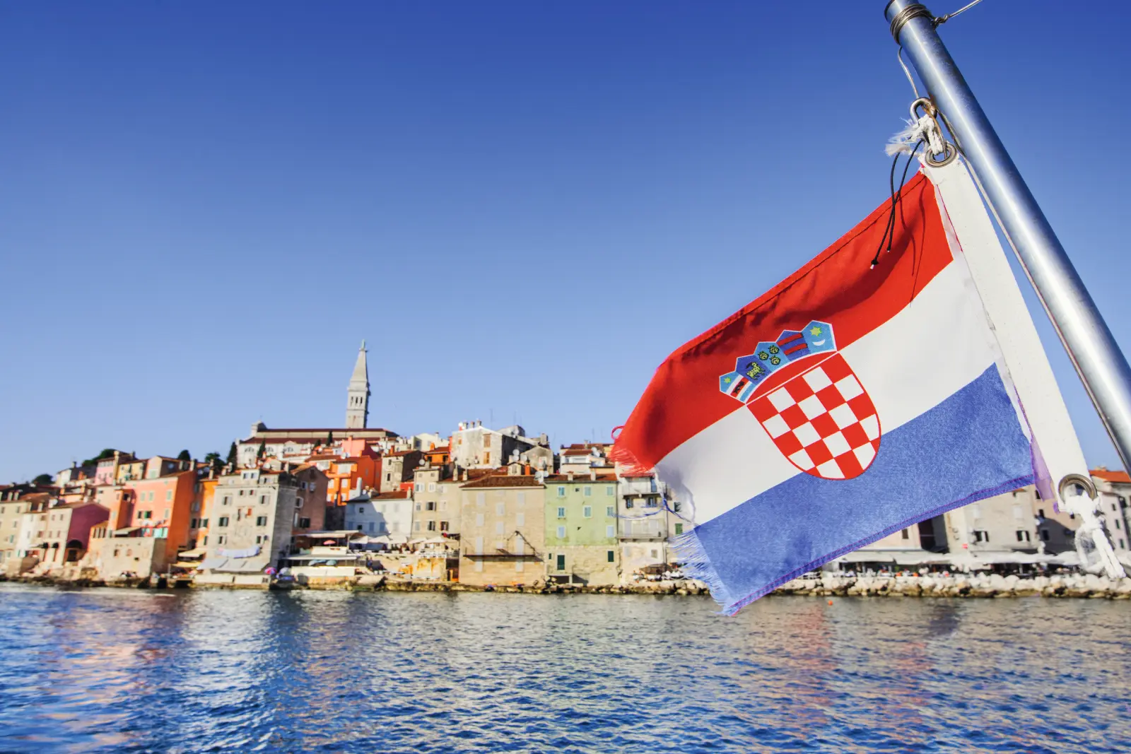 Kroatische Flagge weht vor Küstenstadt mit Kirchturm im Hintergrund.