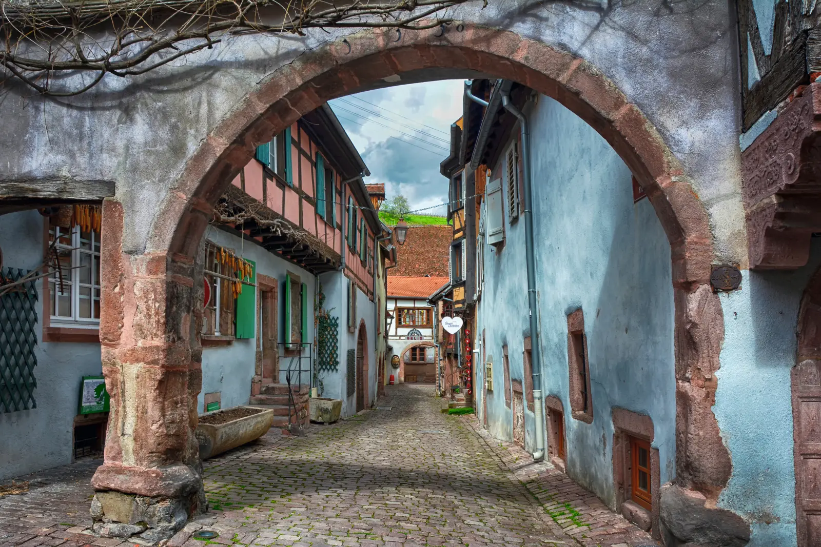 Cobbled old town lane with historic half-timbered houses and a stone archway.