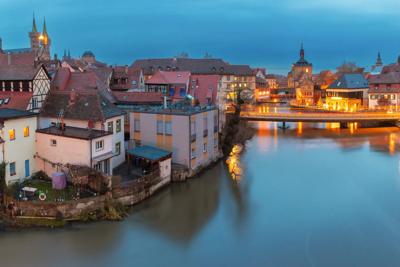 Veduta della città con fiume ed edifici illuminati al crepuscolo.