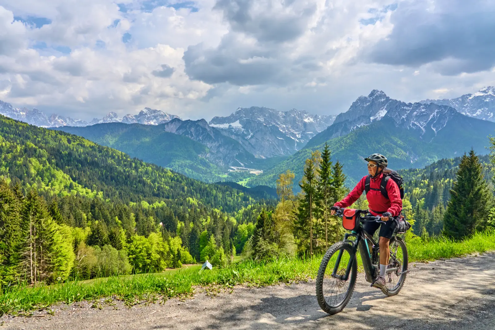 Ciclista su un sentiero di montagna con le Alpi sullo sfondo.