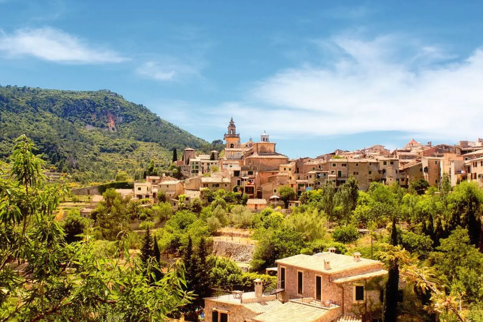 Villaggio medievale in un paesaggio collinare sotto un cielo azzurro.