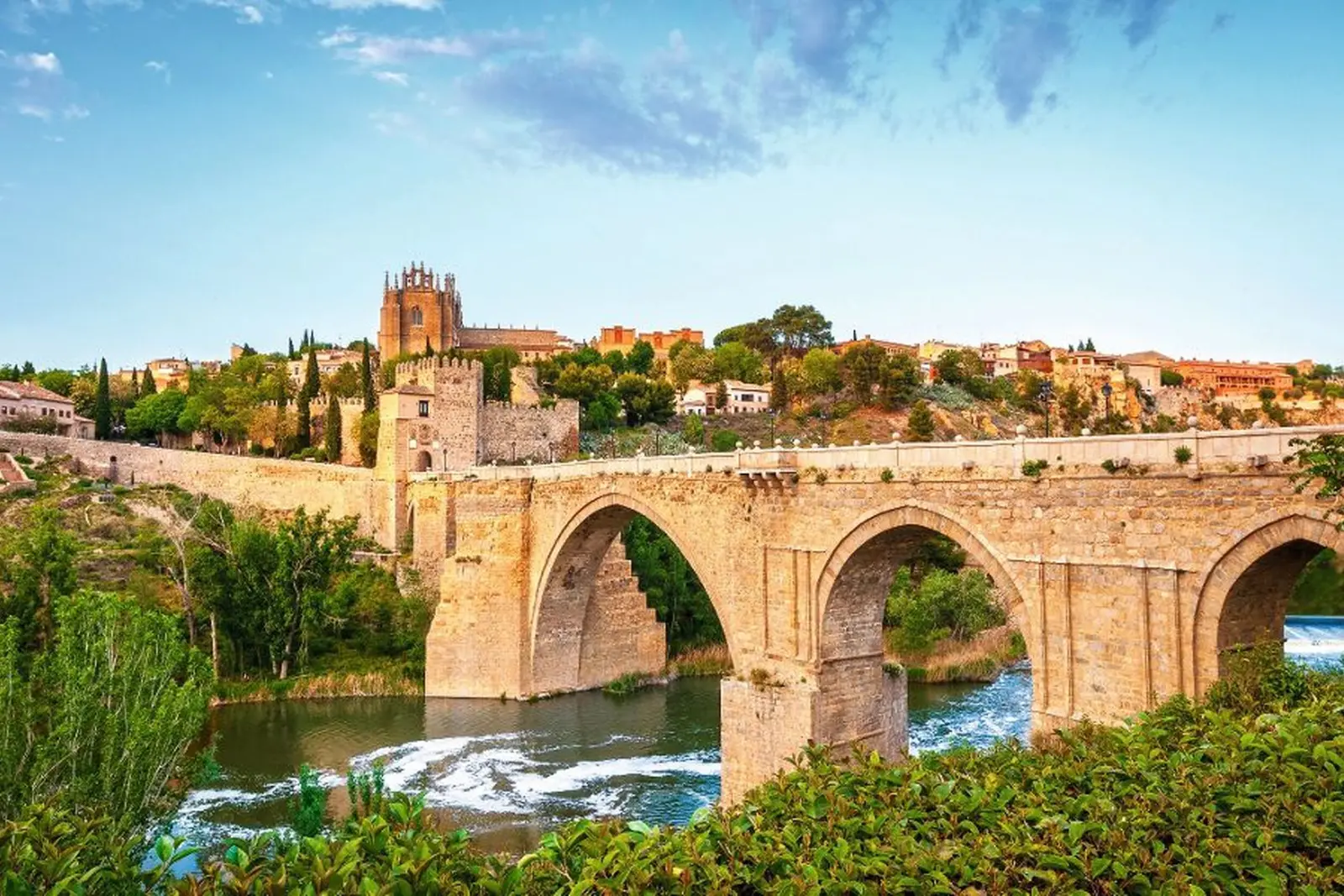 Ponte di pietra su un fiume con architettura storica sullo sfondo.