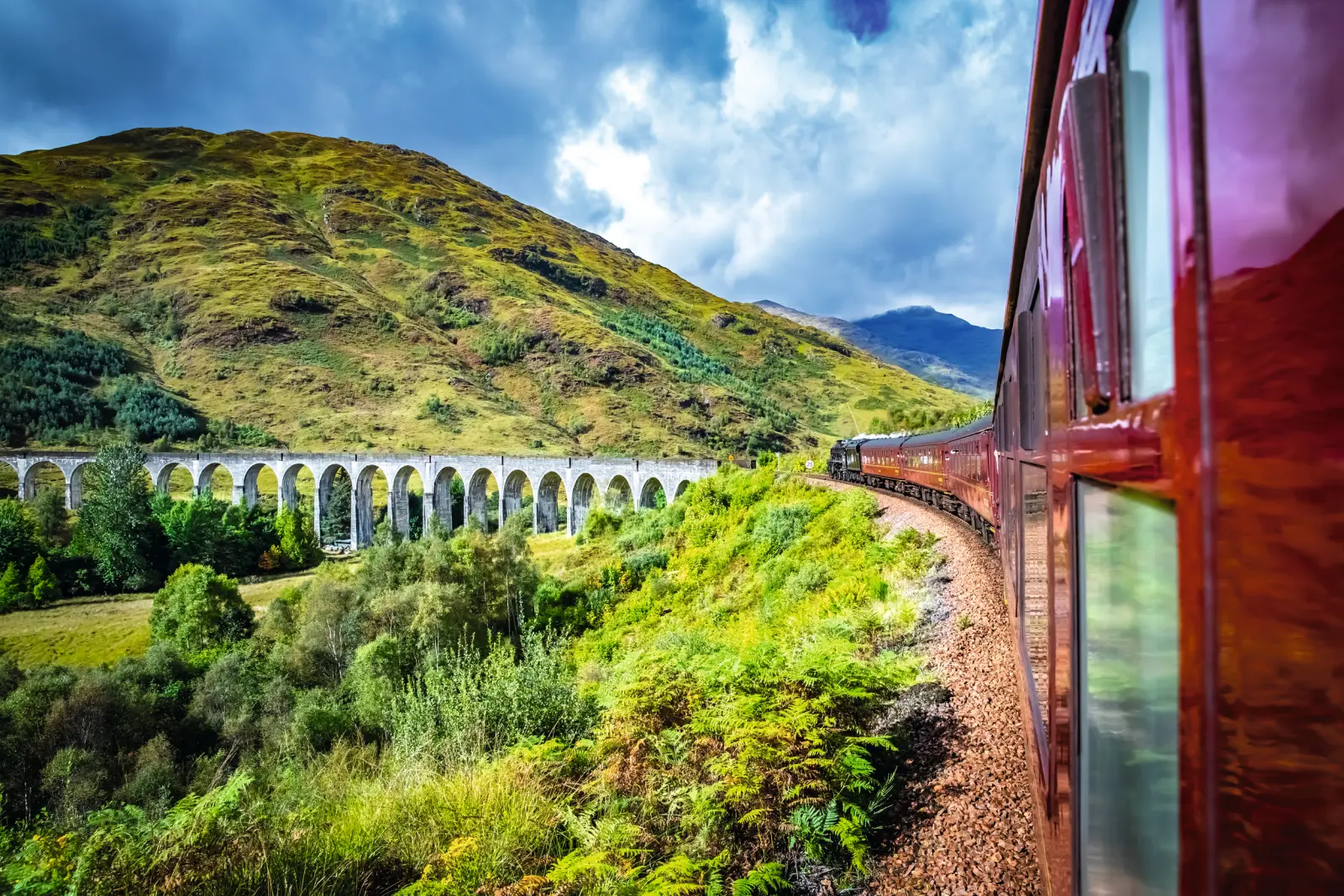 Treno che attraversa un viadotto in un paesaggio collinare verde.