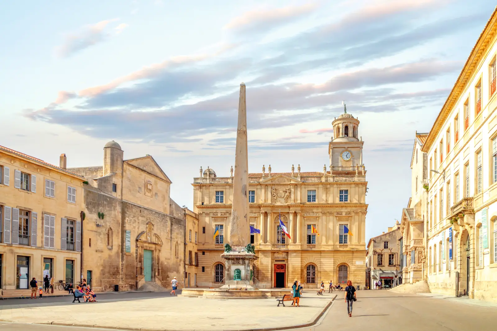 Historic square with an obelisk and old buildings at sunset.