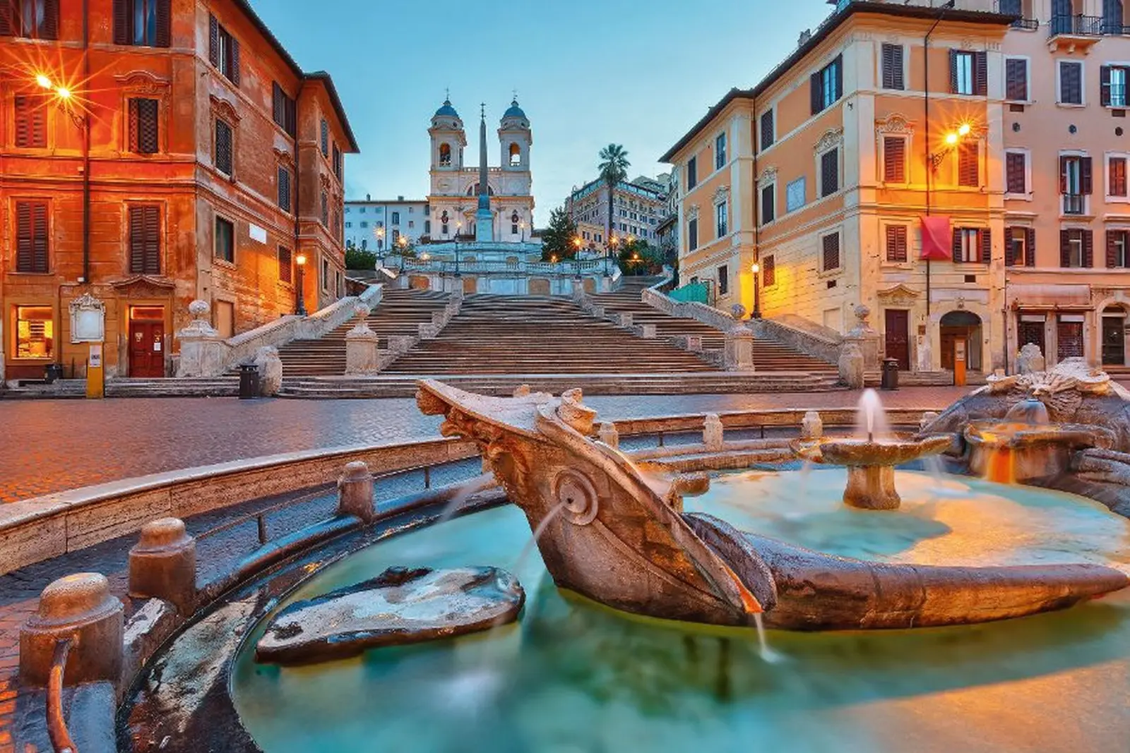 Platz mit Brunnen und Treppe bei Dämmerung in einer historischen Stadt.