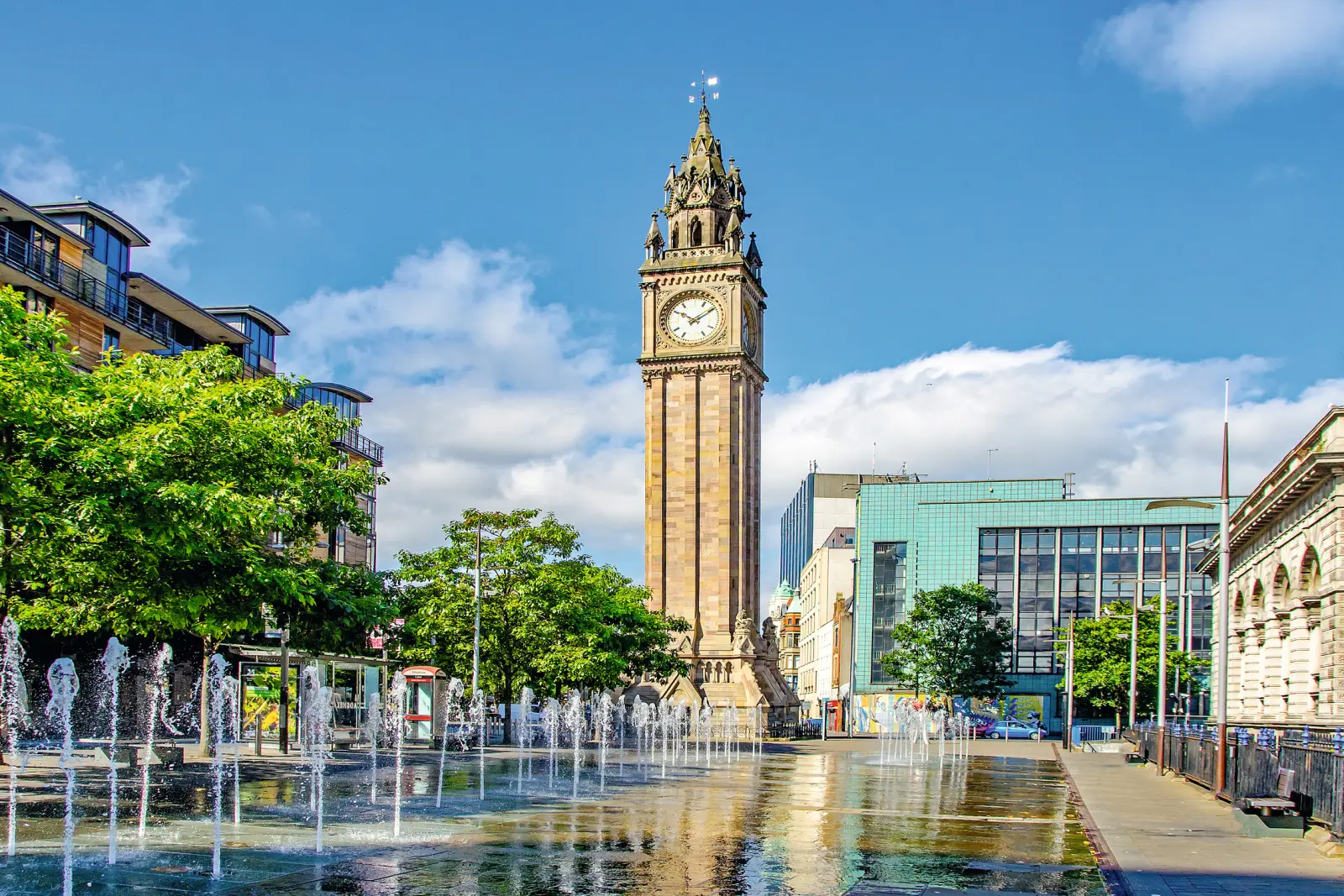 Historic clock tower with water features and buildings in the background on a sunny day.