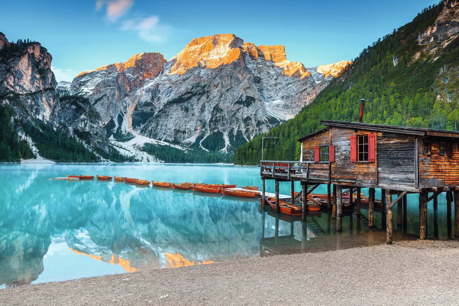 Lake Prags (Pragser Wildsee) in the Dolomites, South Tyrol, Italy, with a jetty, a wooden boathouse and boats on the clear water, surrounded by majestic Alpine mountains.