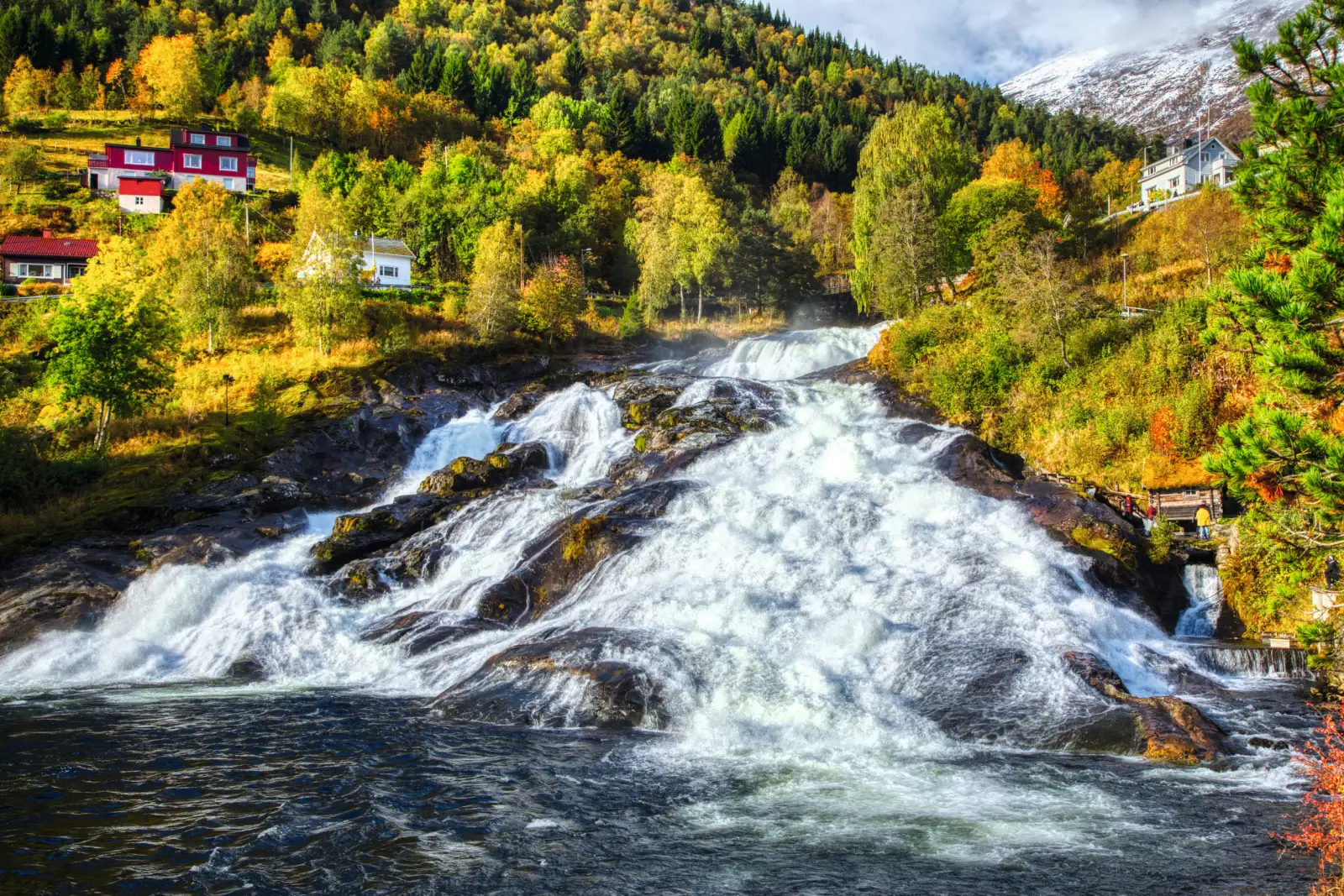 Waterfalls in Hellesylt in autumn, surrounded by colourful foliage and small houses.