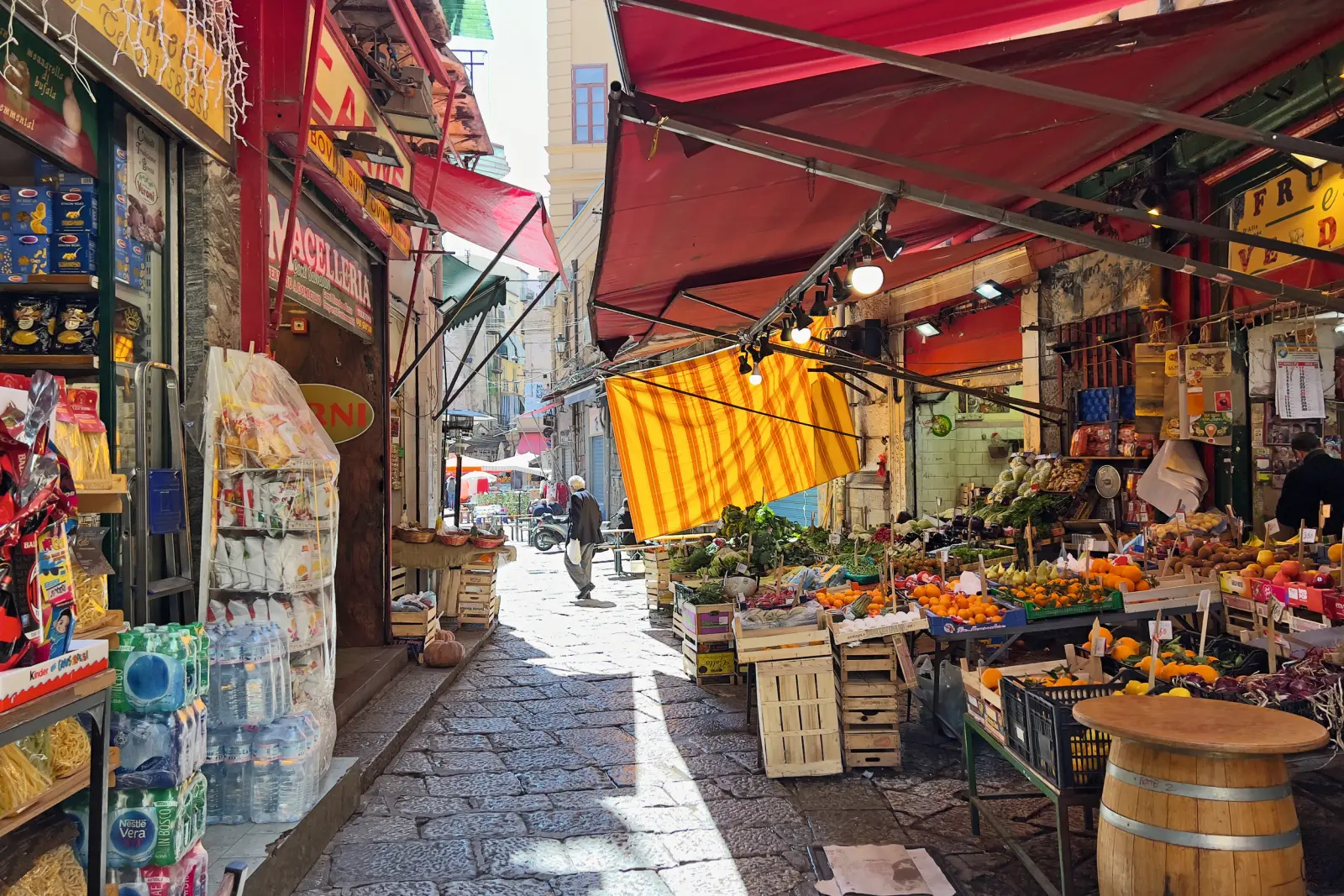 Market street with fruit and vegetable stalls under red parasols.