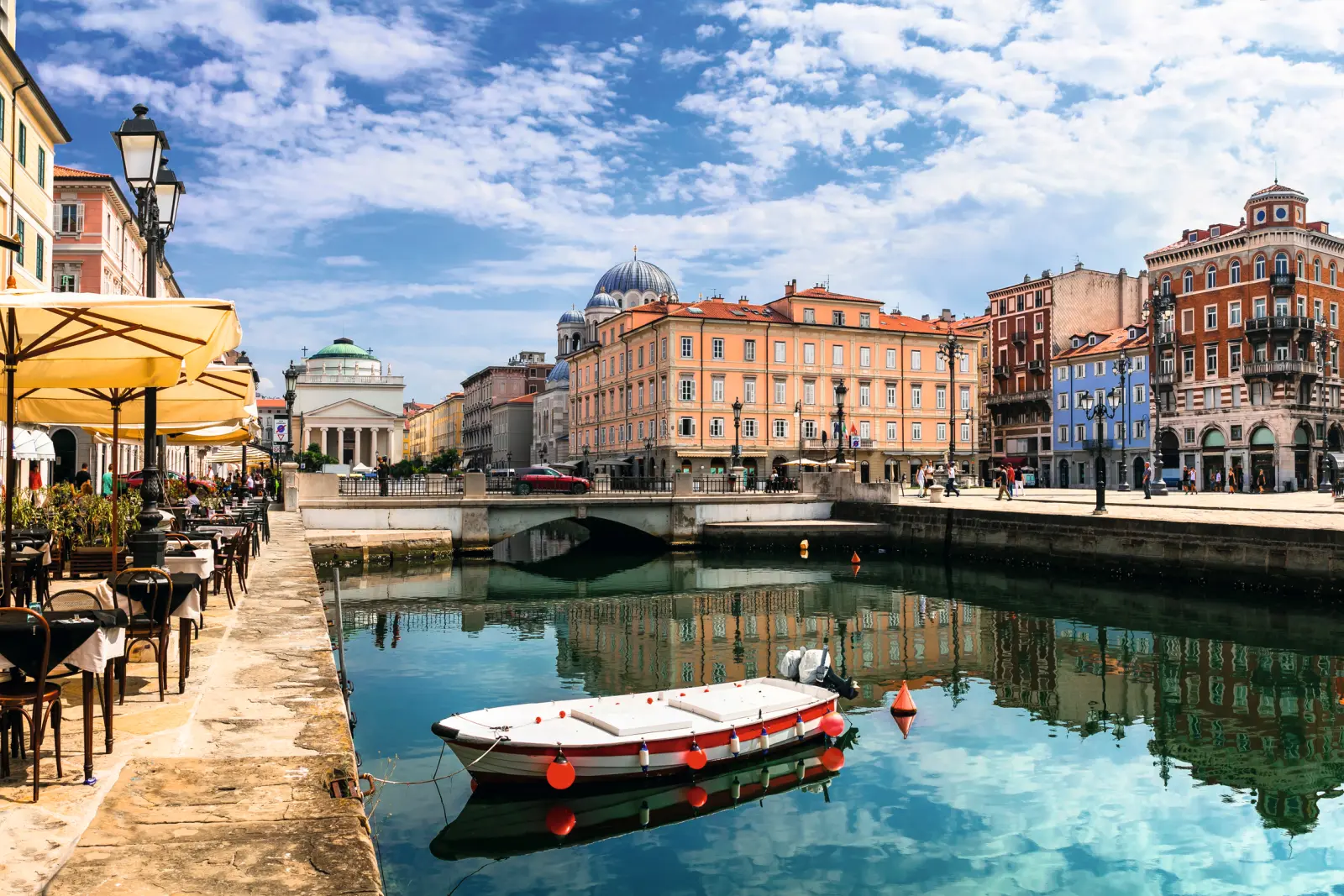 Canale con barca, circondato da edifici storici e caffè all'aperto sotto un cielo azzurro.