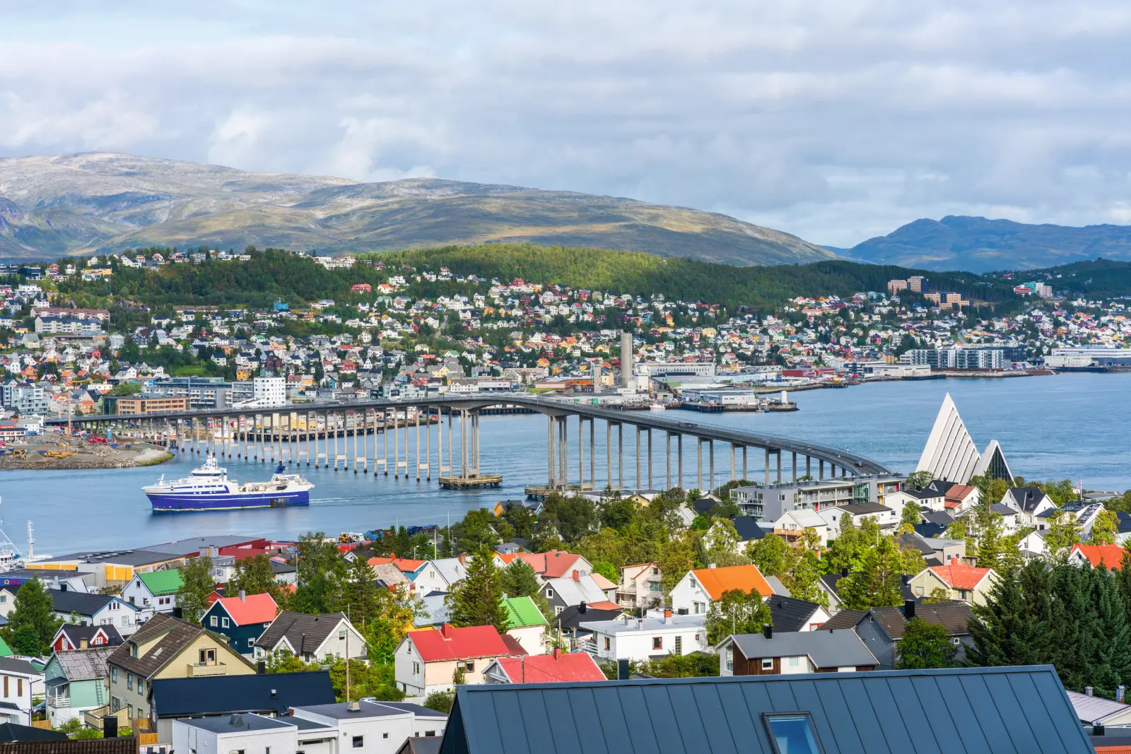 Coastal town with a bridge, a ship and mountains in the background.