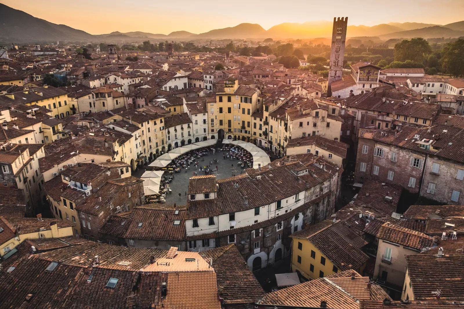 Aerial view of a piazza in an Italian town at sunset, surrounded by rooftops.