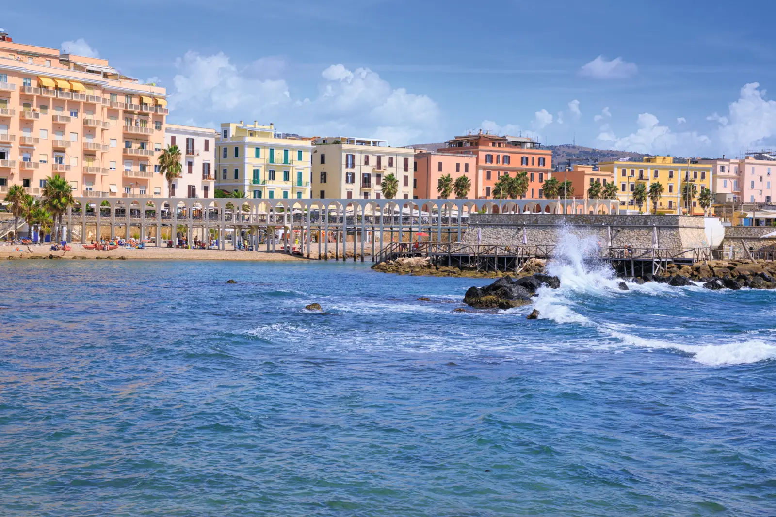 Coastal town with colourful buildings and waves lapping the shore.
