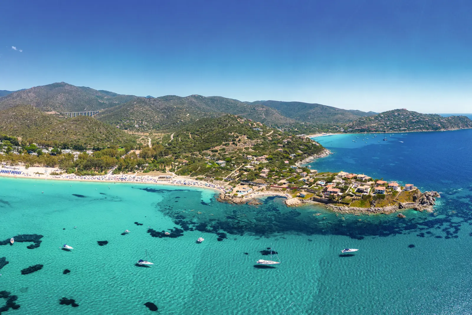 Vue aérienne d’un littoral avec mer bleue et plusieurs bateaux.
