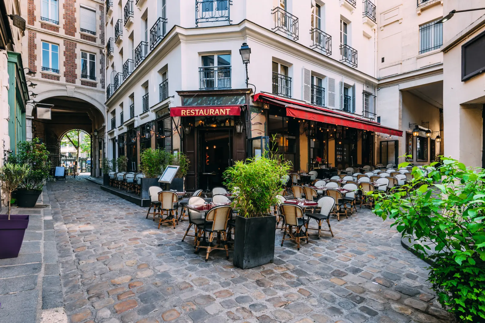 Restaurant de rue avec stores rouges et tables sur une rue pavée.