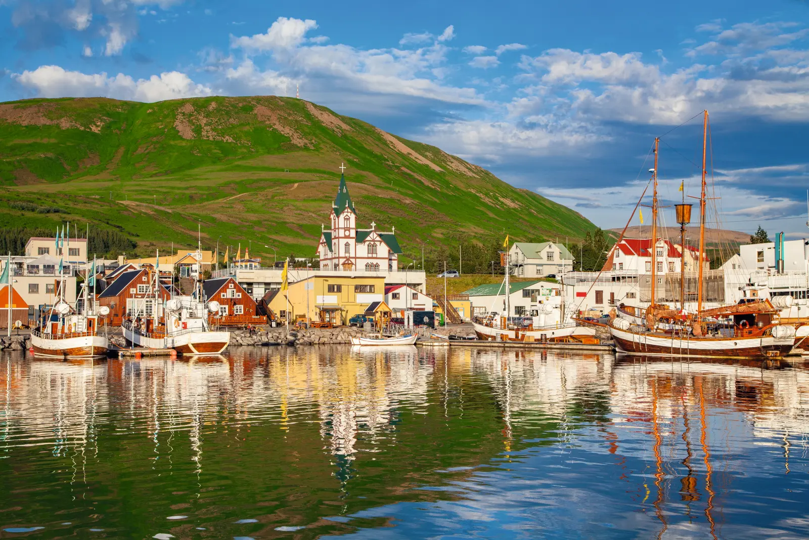 Harbour with colourful buildings and boats, green hills in the background under a blue sky