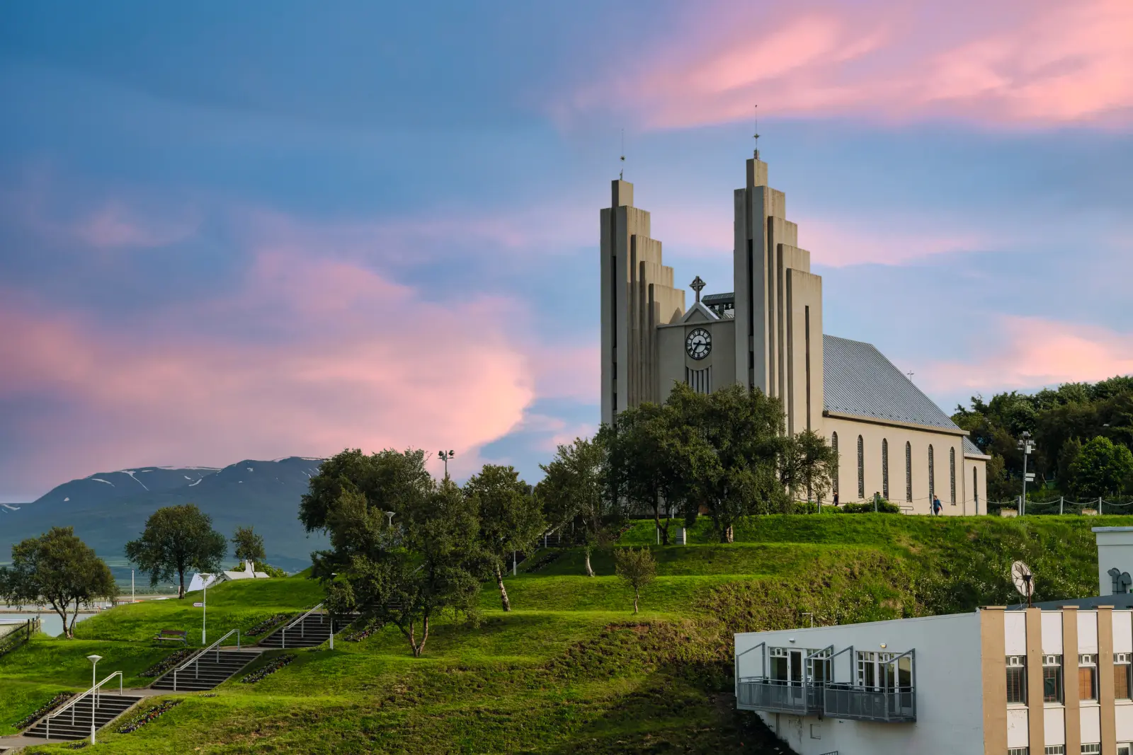 Église sur une colline entourée d’arbres, avec un ciel rose en arrière-plan.