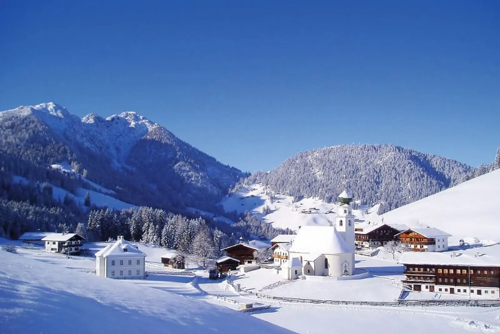 Wintry village scenery in Thierbach, Wildschönau, with snow-covered mountains in the background.