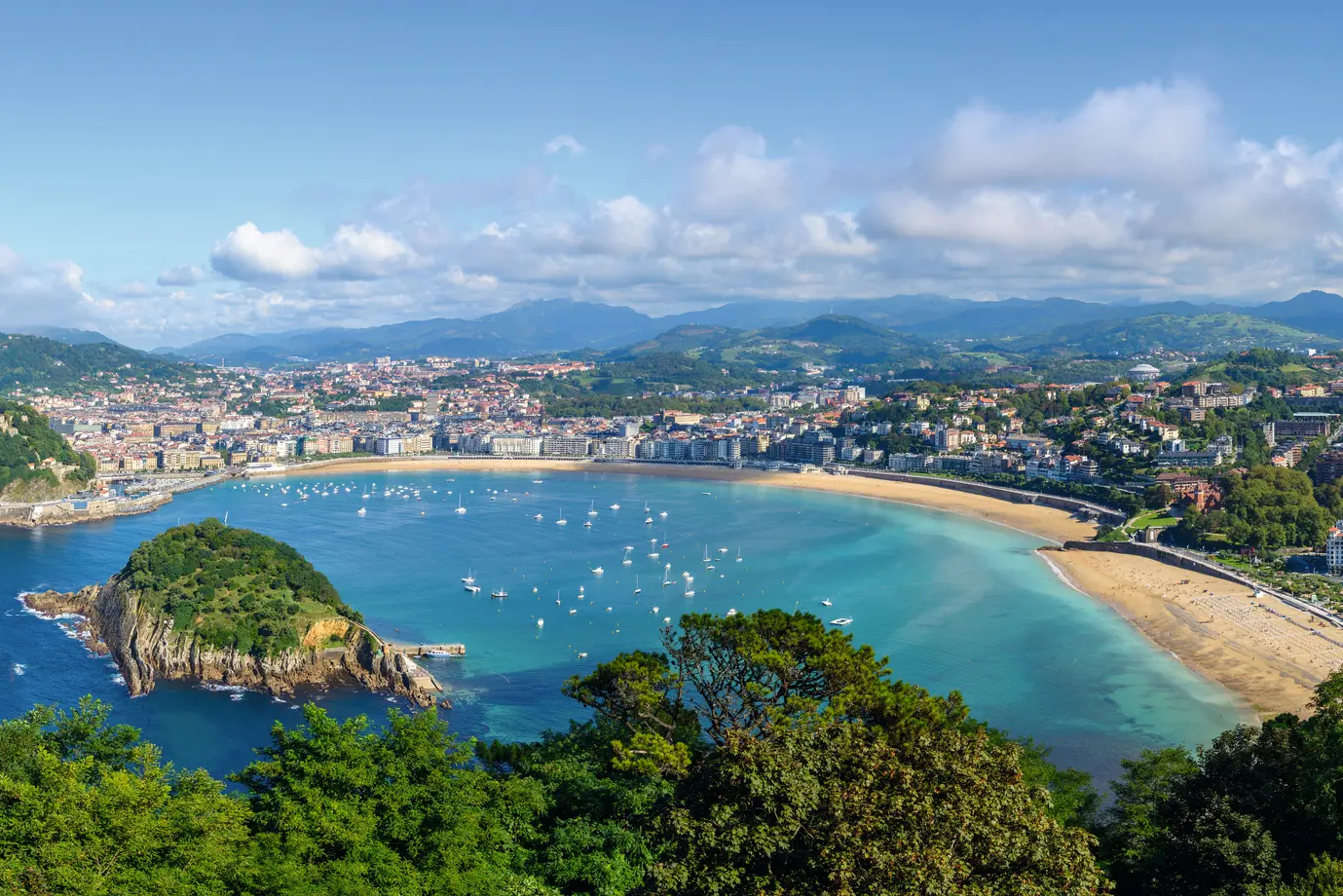 Vista panoramica su una città costiera con spiaggia di sabbia e porto sotto un cielo sereno.