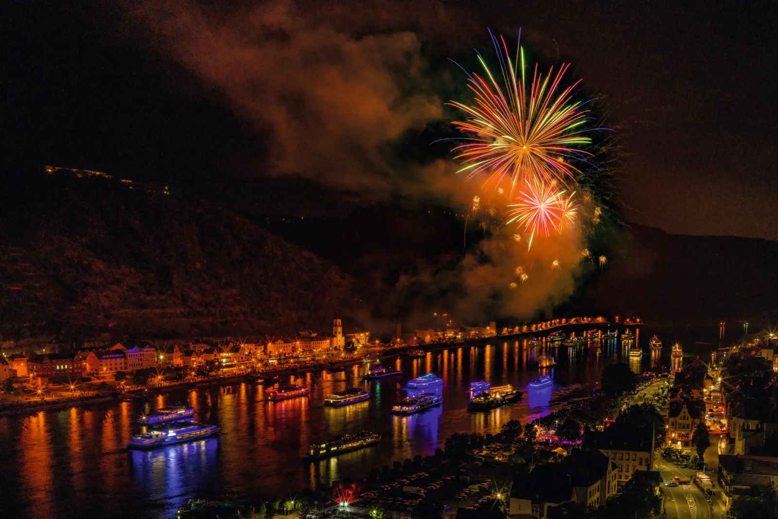 Fireworks above a river, illuminated bridge at night.