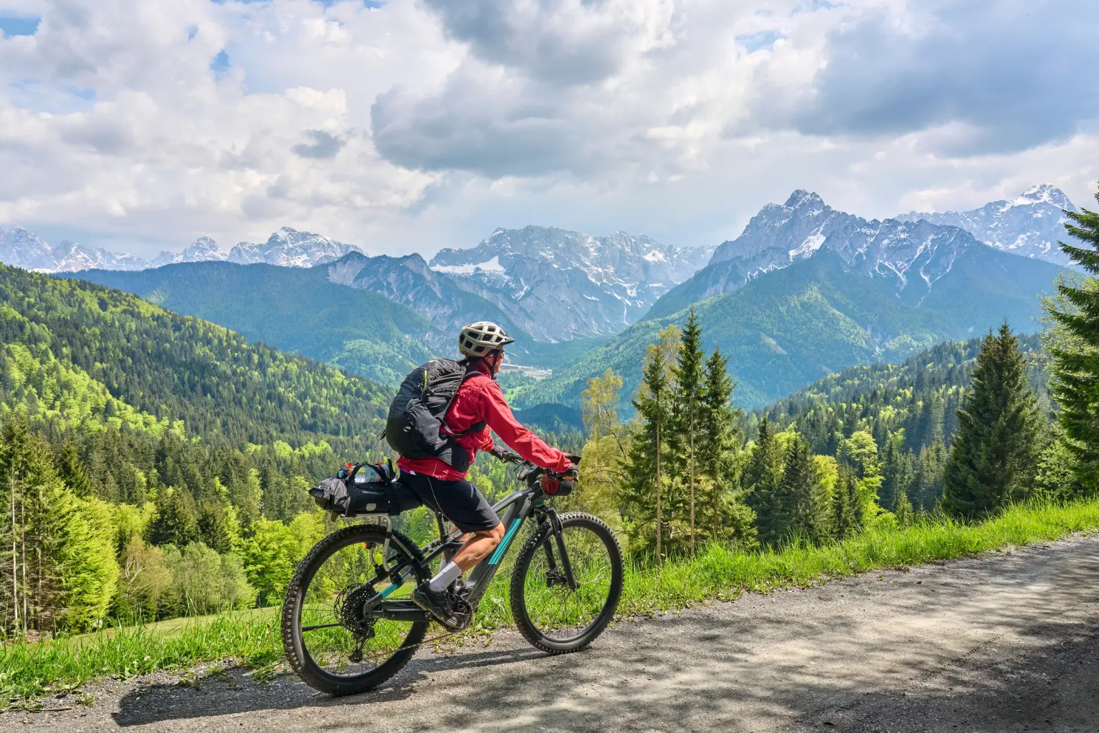 Radfahrer auf einem Bergweg mit Blick auf bewaldete Berge und einen wolkigen Himmel.