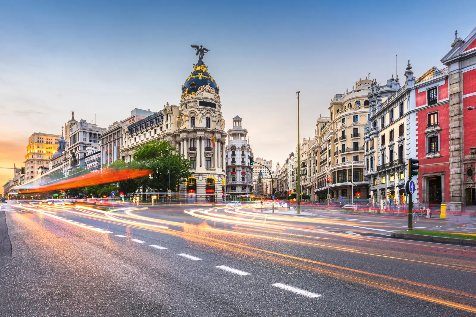Scena di strada a Madrid al tramonto con edifici storici e scie luminose.