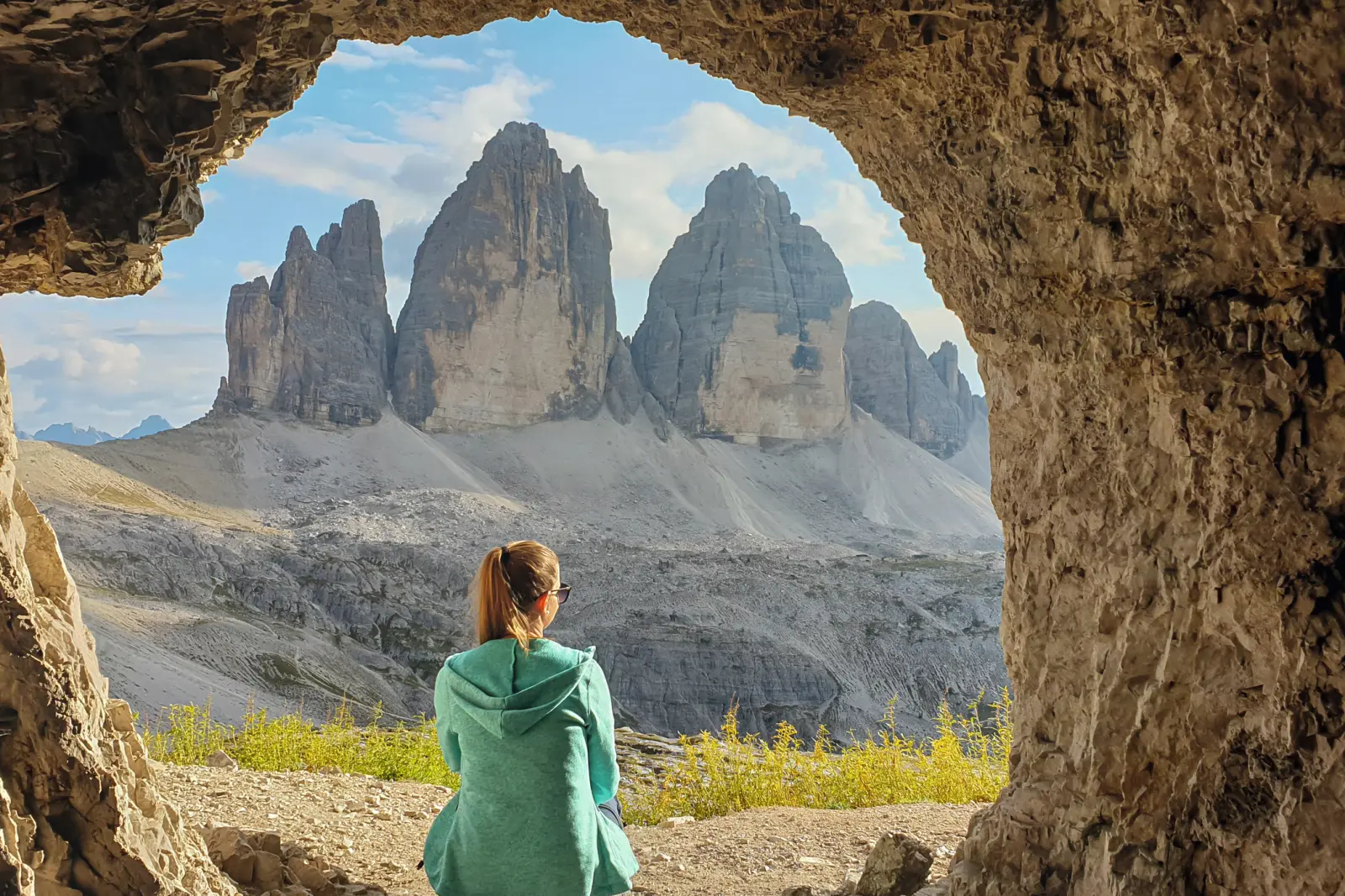 Una donna è seduta all'ingresso di una grotta e contempla le Tre Cime di Lavaredo nelle Dolomiti italiane.