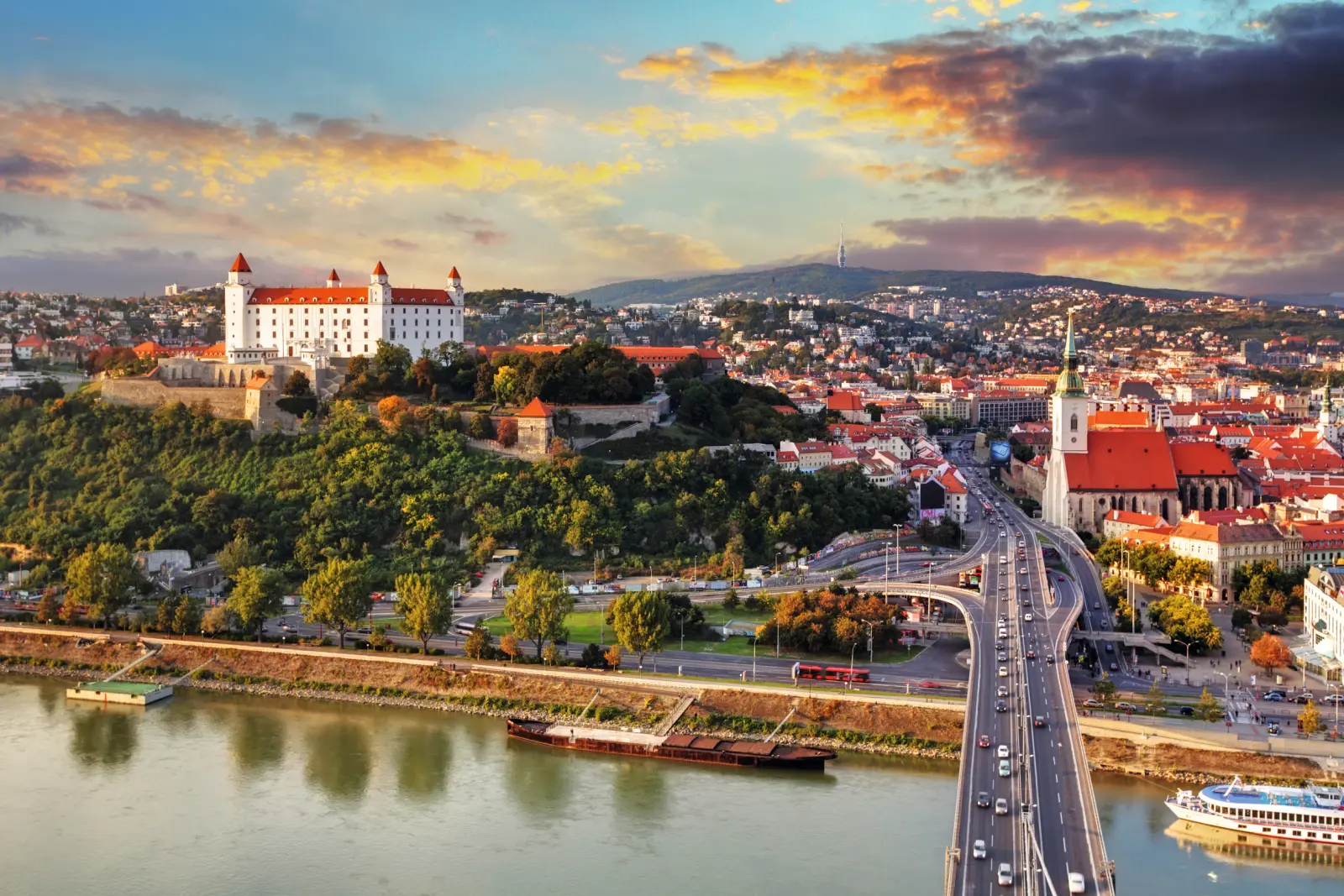 Stadtansicht von Bratislava mit Burg und Fluss bei Sonnenuntergang.