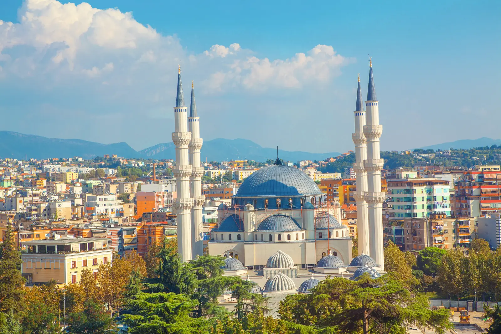 Large mosque with four minarets against a backdrop of the town and mountains.
