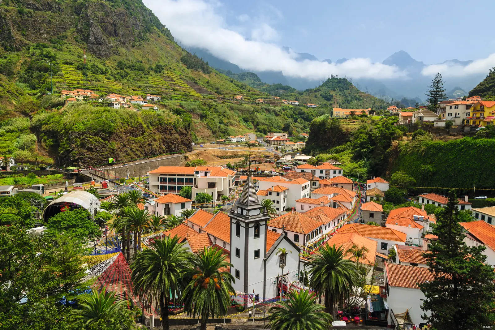 Mountain village with a white church and red roofs, surrounded by green hills and mountains.
