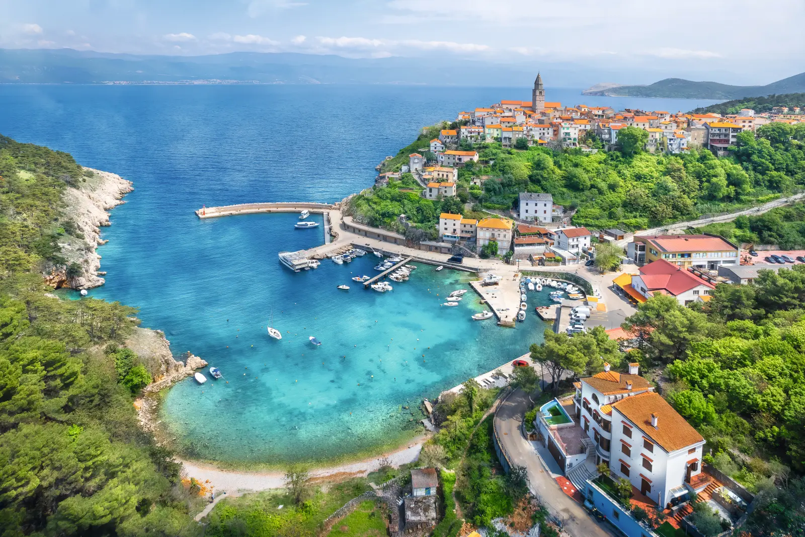 Coastal town with a bay, boats and colourful buildings on a hill in a sunny landscape.