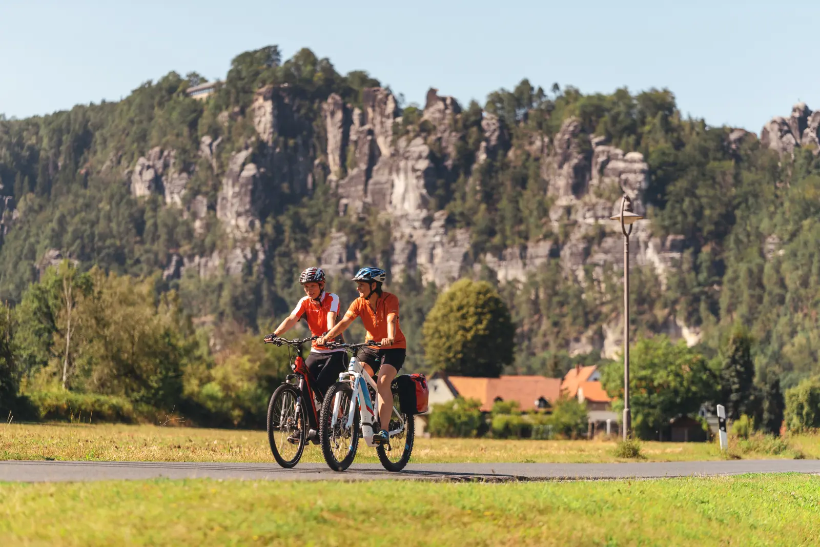 Due ciclisti percorrono un sentiero davanti a pareti rocciose nella località termale di Rathen.