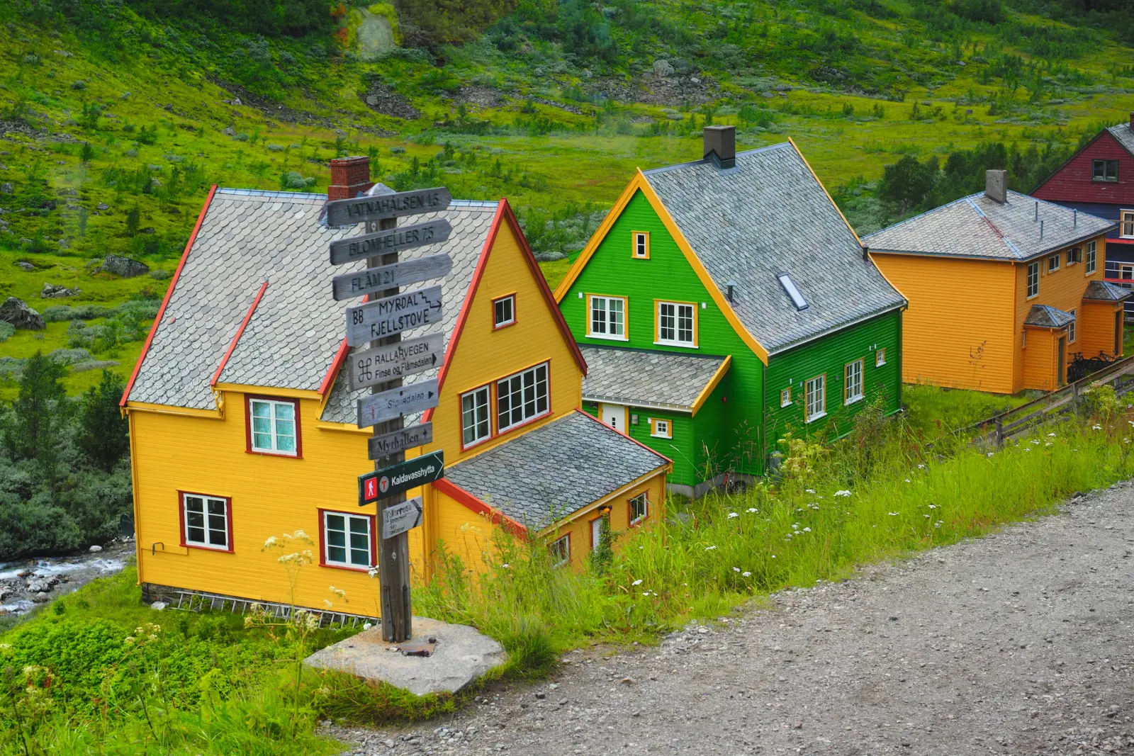 Colourful wooden houses in a rural landscape with a path and trees.