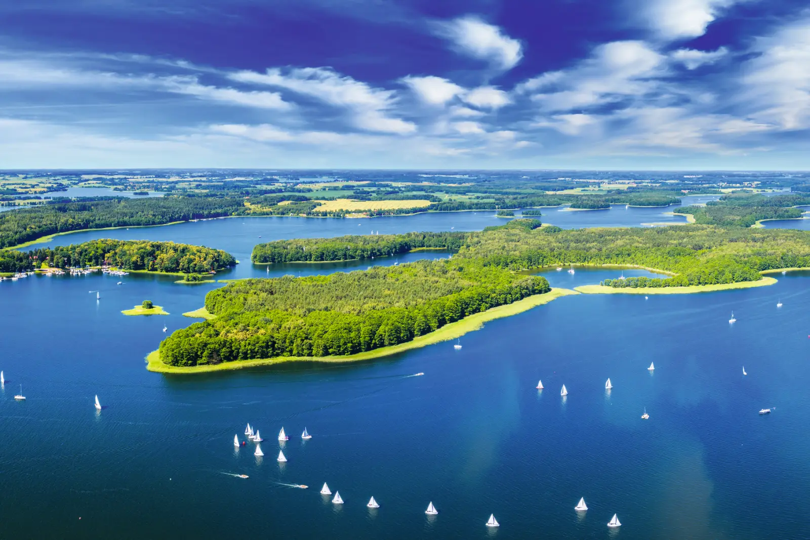 Vue aérienne d’un lac avec des îles et de nombreux voiliers sous un ciel bleu.