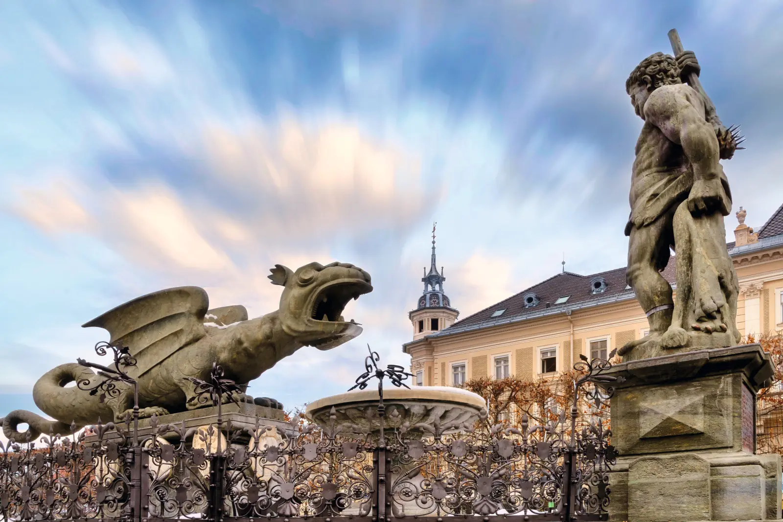 Stone statue of a dragon and a man in front of a backdrop of historic buildings.
