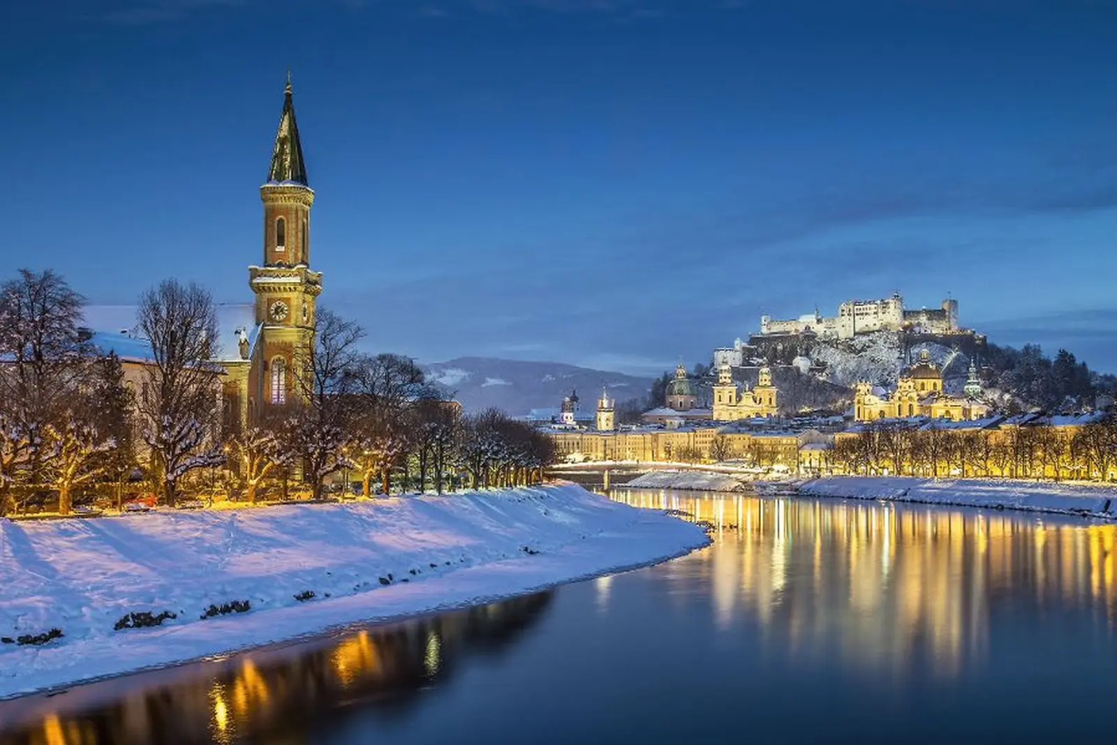 Veduta invernale di Salisburgo al crepuscolo, con neve e fiume illuminato.