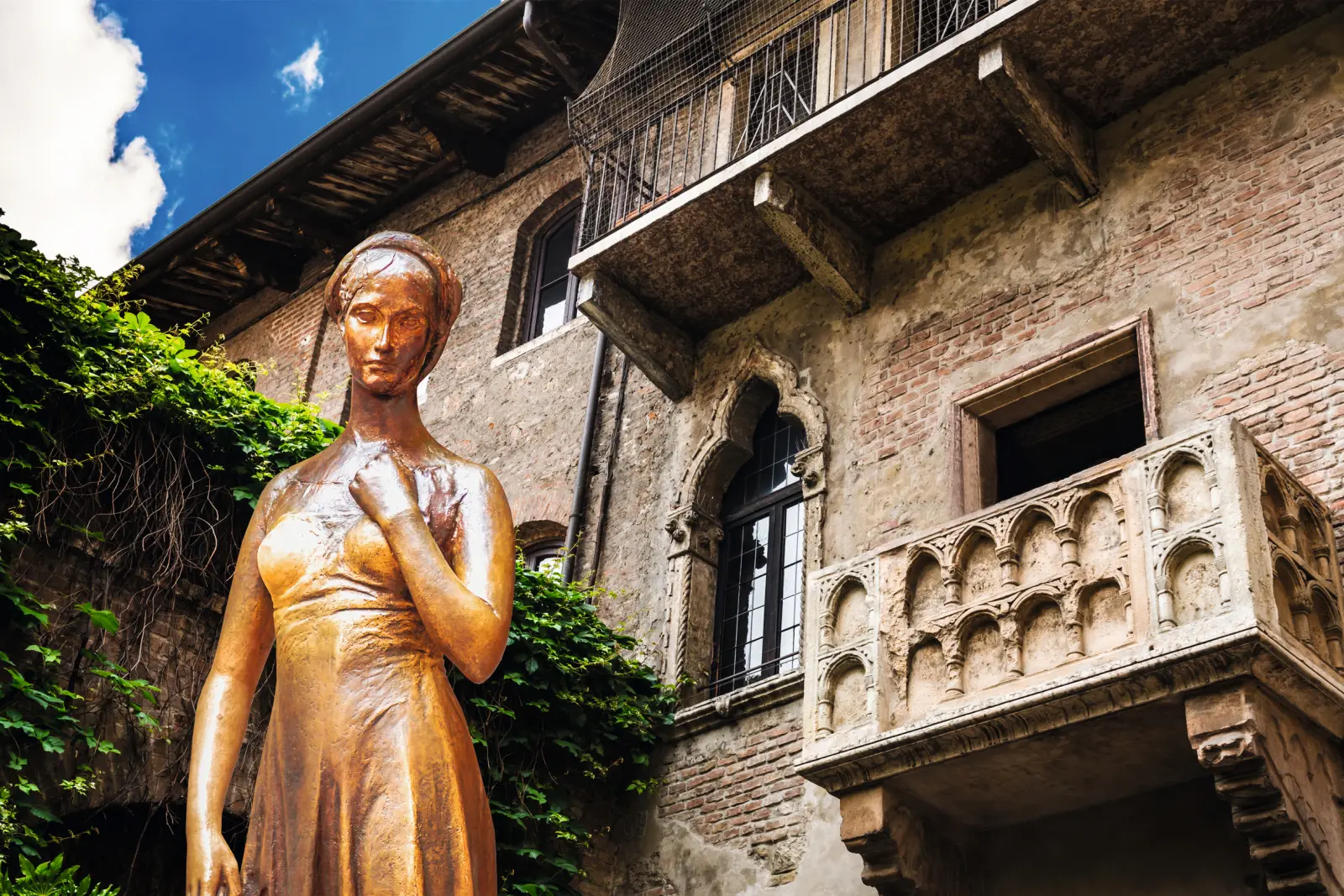Statue d’une femme devant un bâtiment historique orné d’un balcon et de lierre.