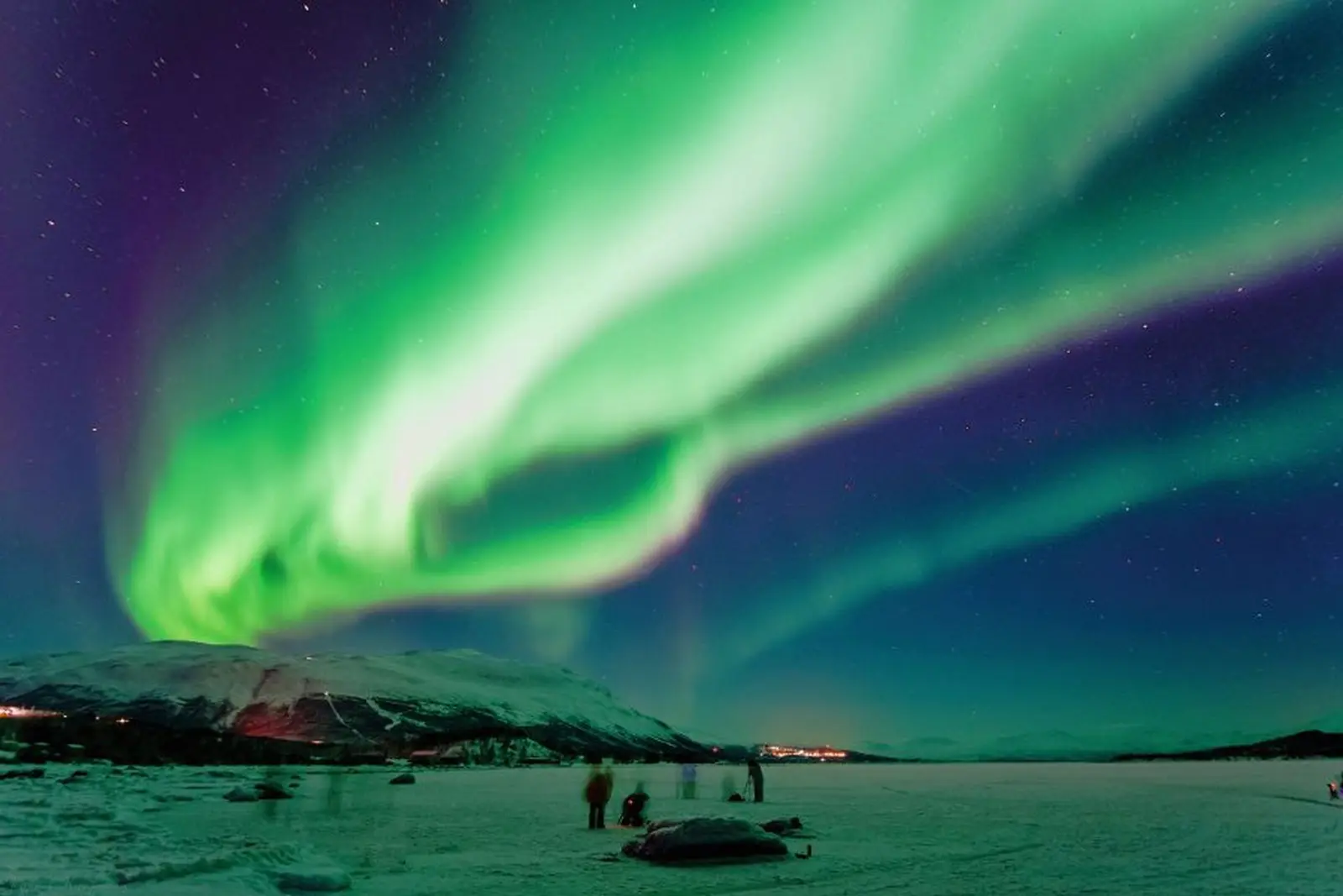 Northern lights above a snowy landscape with people in the foreground.