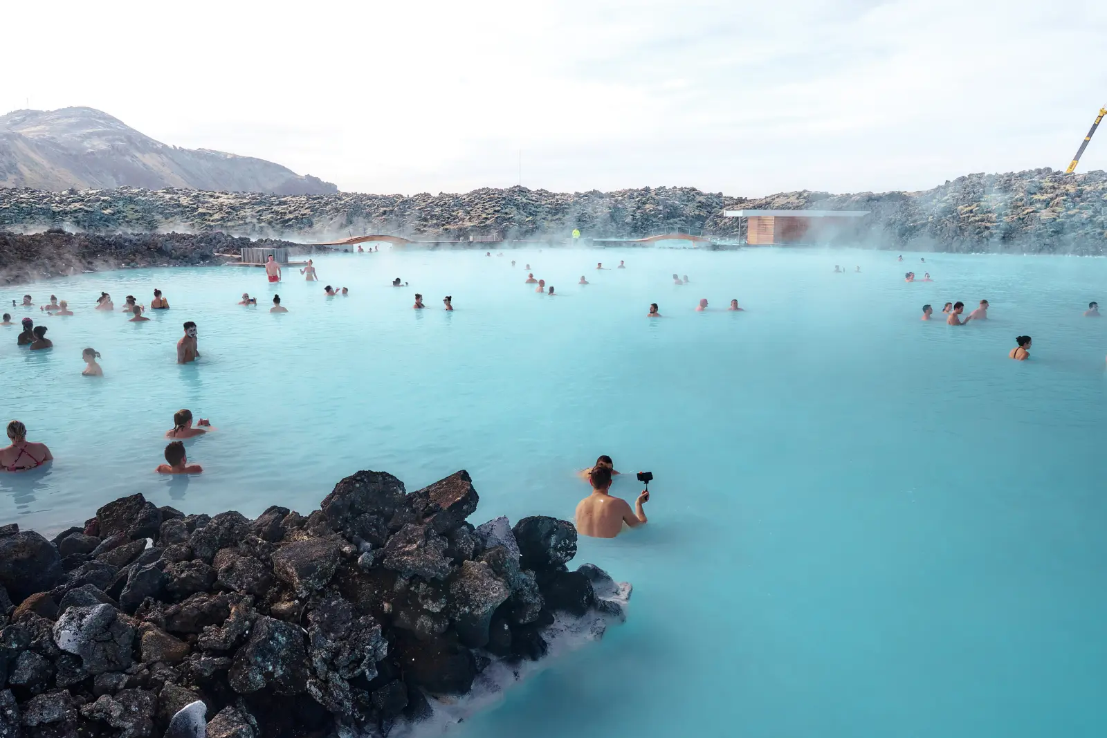 Menschen genießen heiße Quellen in einer blauen Lagune mit Felsen.