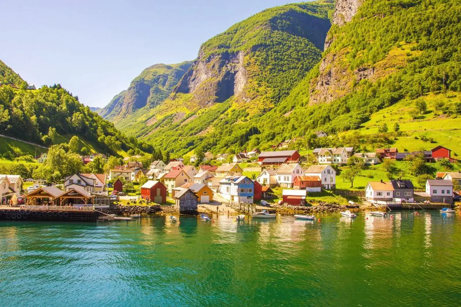 Petit village au bord d’un lac, devant des collines et des montagnes baignées de soleil.