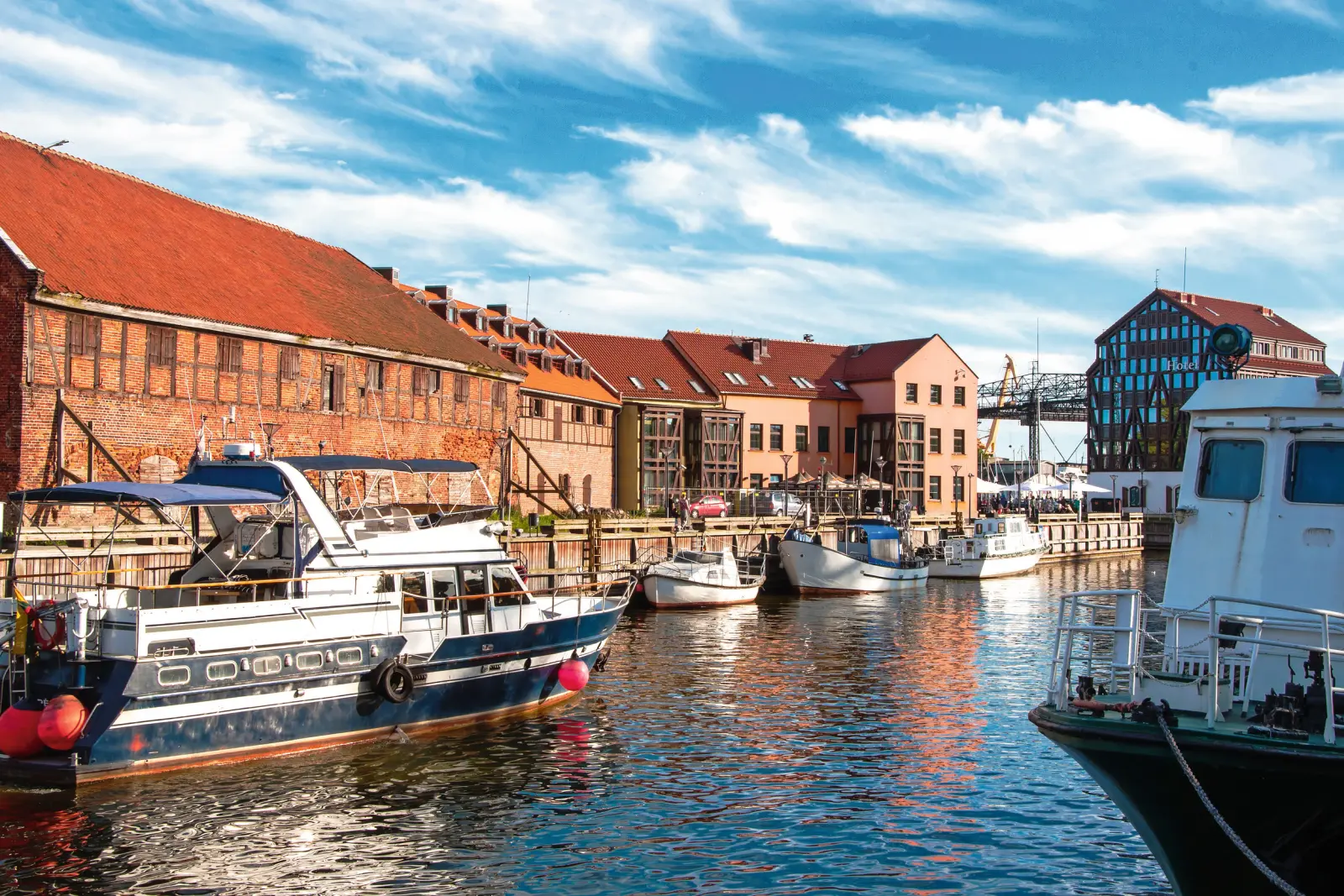 Boats in the historic harbour in front of old brick buildings under a blue sky.