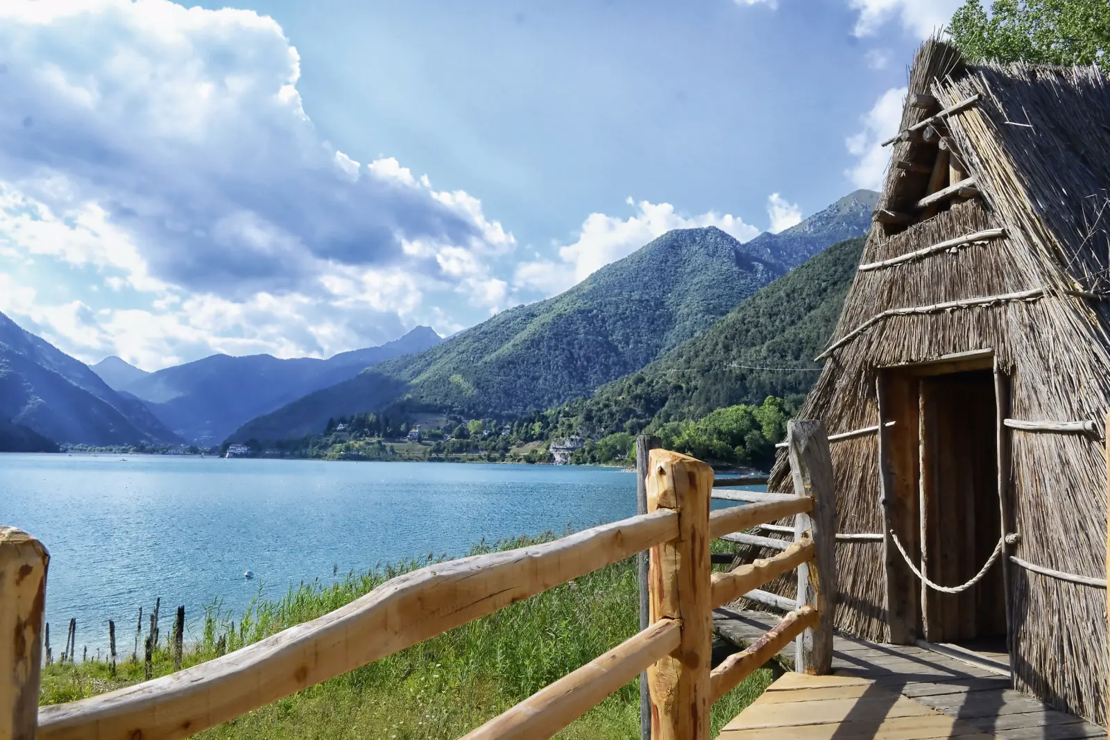 Straw hut by the lake with a mountain backdrop and cloudy sky behind.