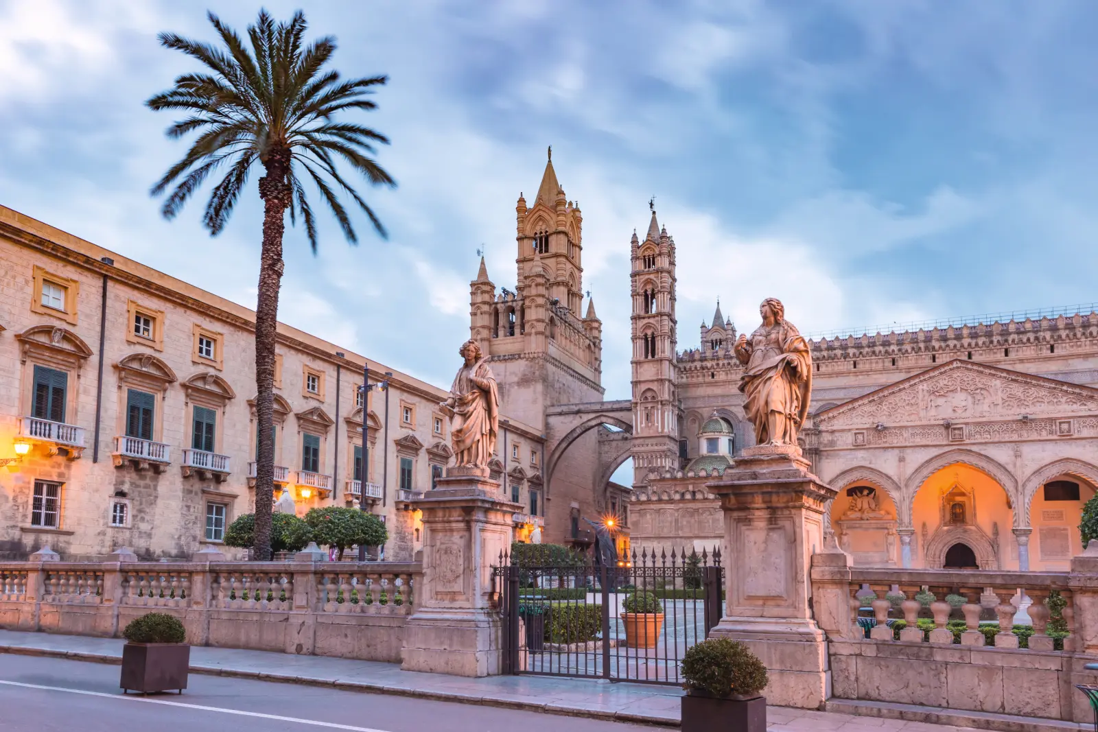Historic cathedral with palm trees and statues in the foreground at sunset