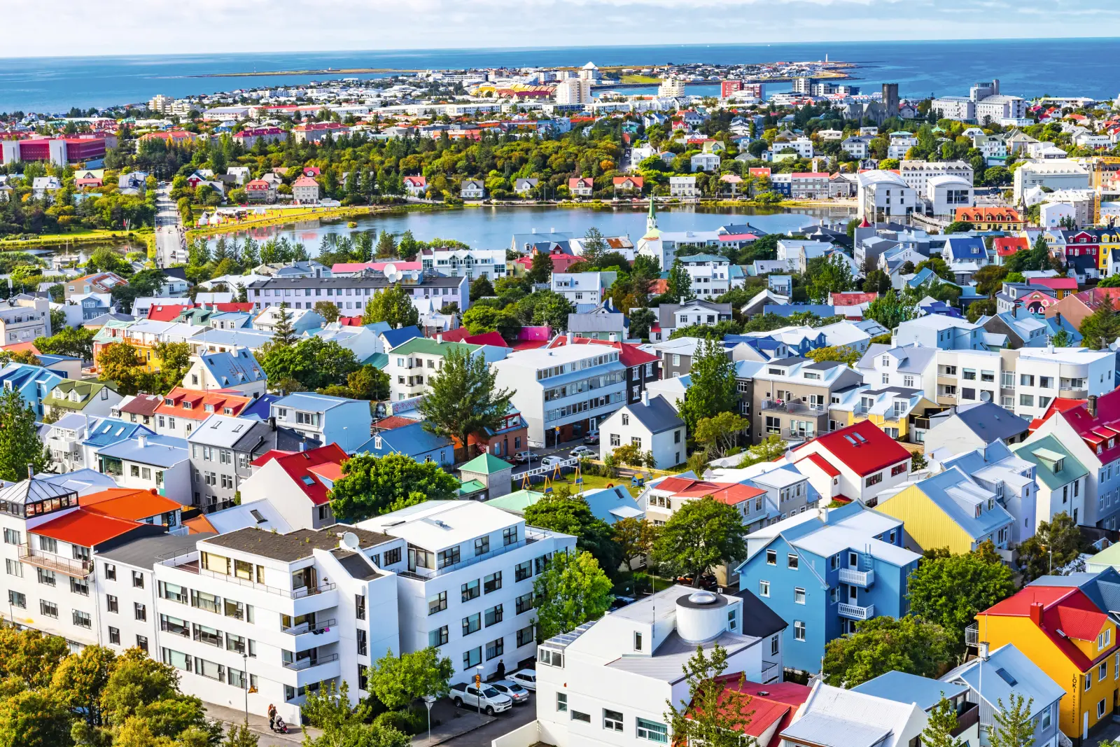 Stadtpanorama mit bunten Häusern, Bäumen und einem See im Hintergrund.