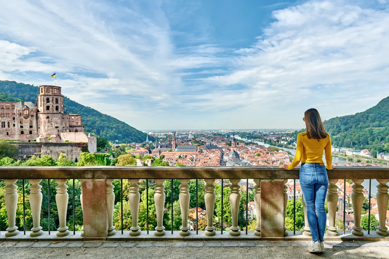 Donna sul balcone con vista su una città storica e su un castello.