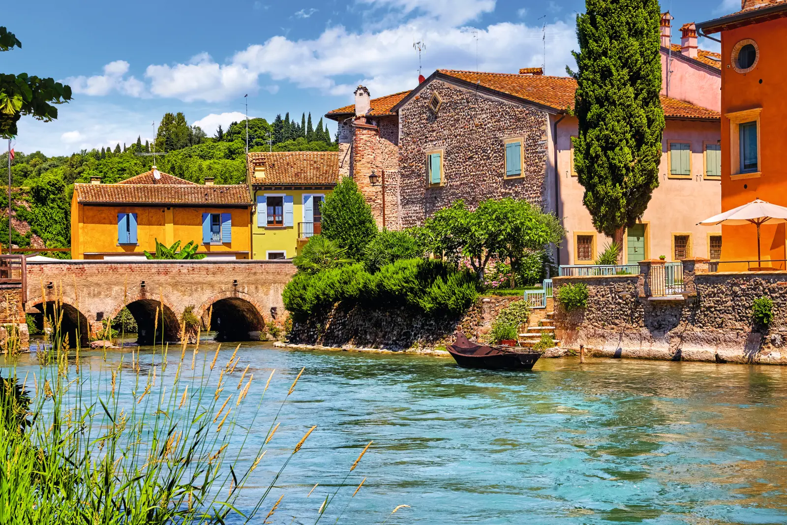 Rivière bordée de vieux bâtiments avec un pont à l’arrière-plan par temps ensoleillé.