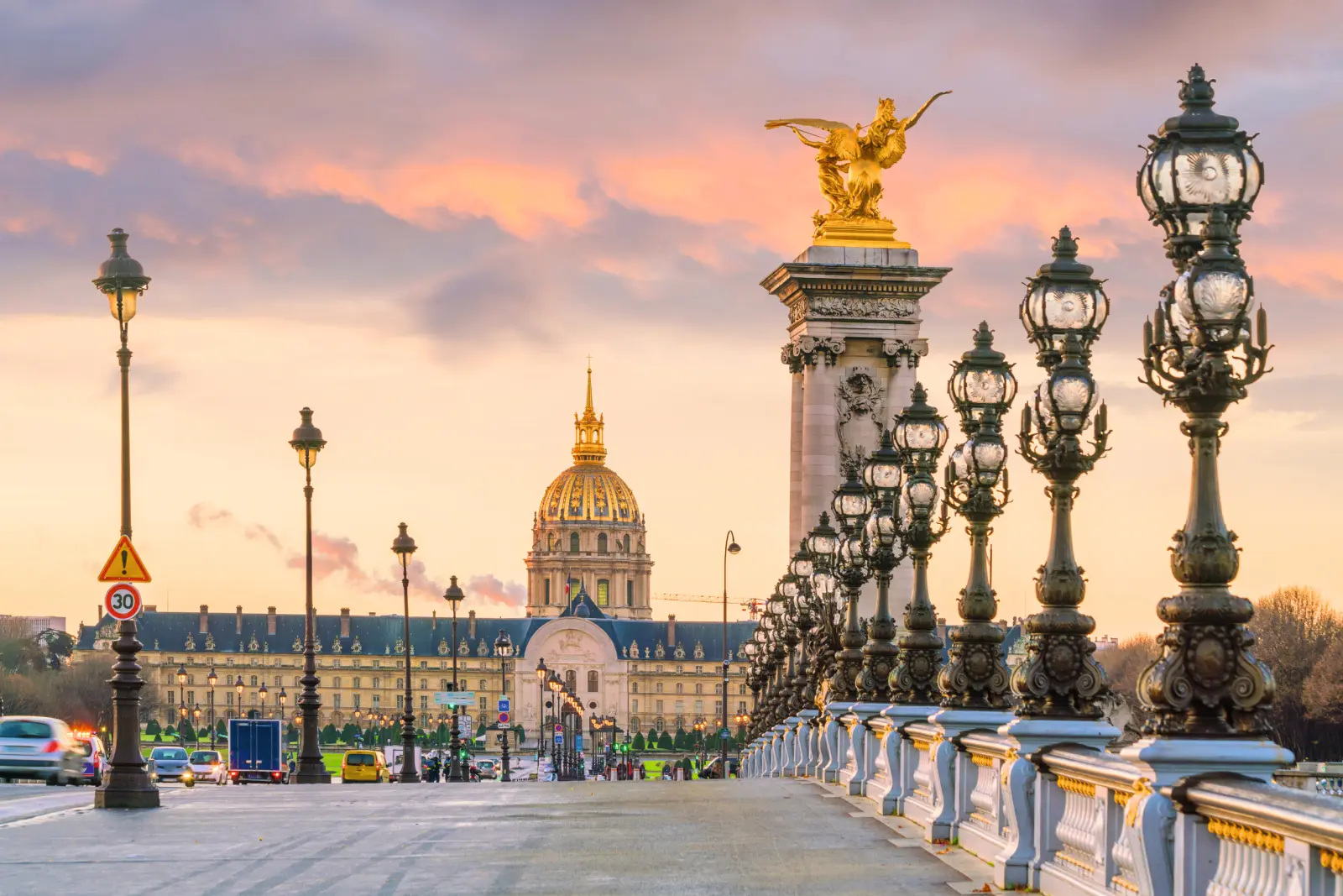Vue sur le pont Alexandre III à Paris au coucher du soleil, avec les Invalides en arrière-plan.